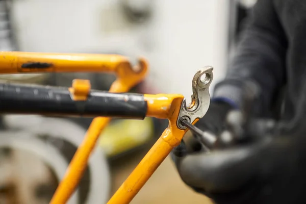 stock image Repair of a bicycle: hands of an unrecognizable person using gloves disassembling an orange bike in his workshop. Selective focus composition.