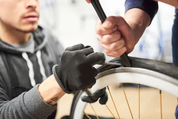 stock image Two men working together collaboratively to remove an airless tire from a bicycle wheel at a bike repair shop. Selective focus composition with copy space.