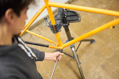 Bisiklet tamircisi onu boyamak için turuncu bir bisikleti söküyor, çerçevenin rengini değiştiriyor, tamirhanesinde..