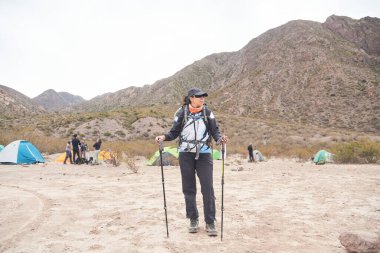 Latin kadın yürüyüşçü sırt çantası ve yürüyüş direkleriyle Potrerillos, Mendoza, Arjantin 'deki kamp alanından yürümeye hazır..
