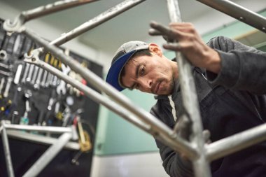 İspanyol bir adam atölyesinde yapılan bisiklet yenileme çalışmalarının bir parçası olarak boyanmamış bir bisiklet çerçevesini zımparalıyor. İşçi yüzüne odaklan..