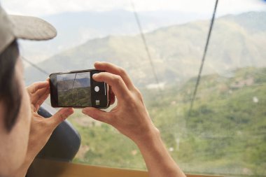 Santander, Kolombiya 'daki Chicamocha Kanyonu' ndaki teleferik kulübesinden telefonuyla fotoğraf çeken tanınmamış bir genç..
