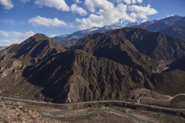 Arjantin 'deki Andean dağlık manzarası, Mendoza nehri ve yol dağlar arasındaki bir vadi boyunca kıvrılır..