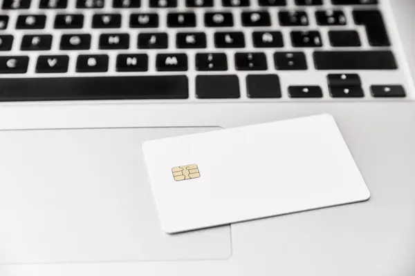 Blank white credit or debit card with microchip on a laptop. Concepts of plastic money and online shopping.