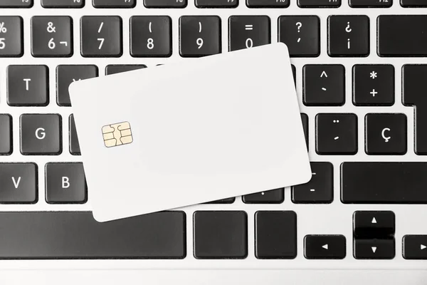 Blank white credit or debit card with microchip on a laptop keyboard. Concepts of plastic money and online shopping. Top view composition without people.