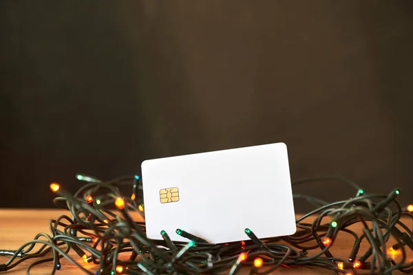 White blank debit or credit card on a string of Christmas lights. Concepts: economy and expenses during the holiday season.