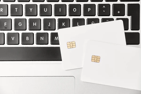 Pair of blank white credit or debit cards on a laptop keyboard. Top view. Concepts of plastic money and online shopping.