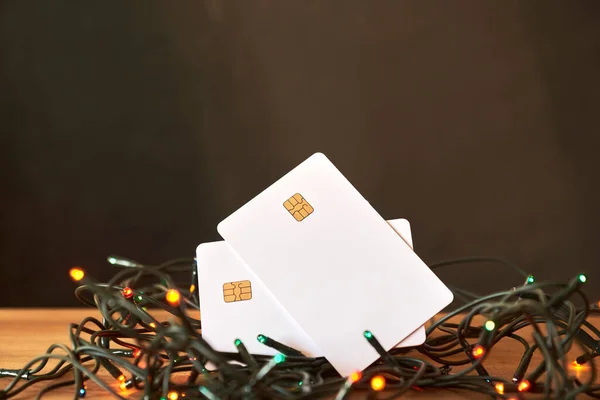Pair of blank debit or credit cards on a string of Christmas lights. Concepts: economy and expenses during the holiday season.
