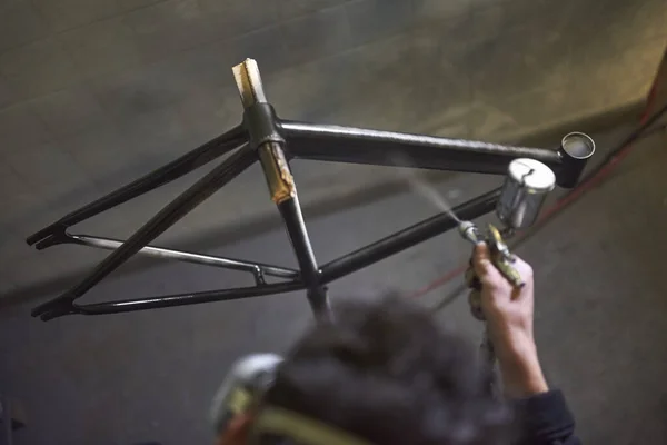 Unrecognizable person spray painting a bicycle frame in his workshop. High angle view composition with copy space.