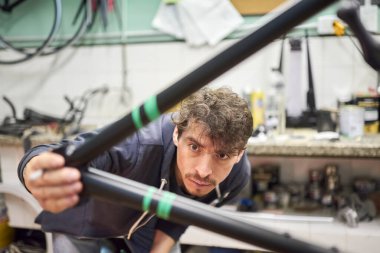 İspanyol genç adam bisiklet atölyesinde özel bir resim tasarımı için özel bir bant ile bisiklet çerçevesi hazırlıyor, el yapımı bir yaratıcı süreç..