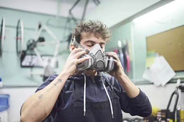 Portrait of a latin young worker removing a respiratory protection mask, as he finishes a spray painting job in his workshop. Health protection in industrial work. Real people working.