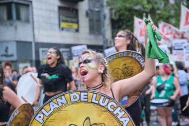 Buenos Aires, Arjantin; 8 Mart 2024: Uluslararası kadınlar grev sırasında elinde yazılı savaş planı ile elinde bir kalkan tutan ve elinde yeşil eşarp sallayan feminist sloganlar atan genç kadın.