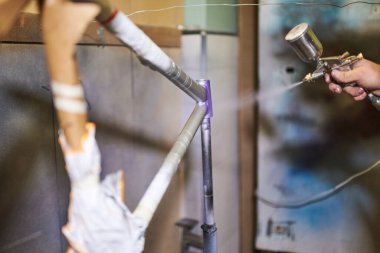 Tanınmayan kişi atölyesinde bisiklet çerçevesi boyuyor..