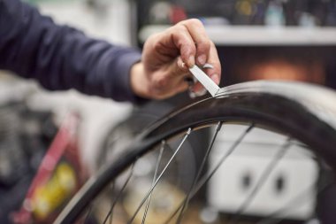 Bisiklet tablosu üzerinde çalışan tanınmayan biri. Tekerlek kenarındaki maskeleme bandını çıkarma zamanı. Görüntüyü kapat.