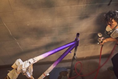 Koruyucu solunum maskesi takan Latin genç adam atölyesinde bisiklet çerçevesi boyuyor. Kopyalama alanı ile seçici odak bileşimi.