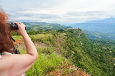 Unrecognizable woman observing from a viewpoint, trough binoculars, Barichara, the most beautiful town in Colombia. clipart