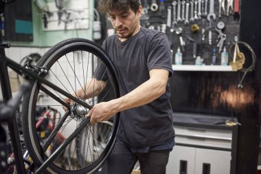 Atölyesinde bir bisikletin arka tekerleğini takan İspanyol tamirci. İş yerindeki gerçek insanlar.