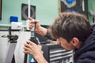 Genç İspanyol bir adam bakım servisinin bir parçası olarak bisiklet atölyesinde bisiklet montajı yapıyor. İş yerindeki gerçek insanlar. Seçici odaklı kompozisyon ve kopyalama alanı.