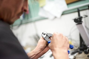 Tamirci, tamirhanesinde bir aletle bisiklet kablosunun ucunu sıkıyor. Seçici odak ve kopyalama alanı ile kompozisyonu kapat. İş yerindeki gerçek insanlar.