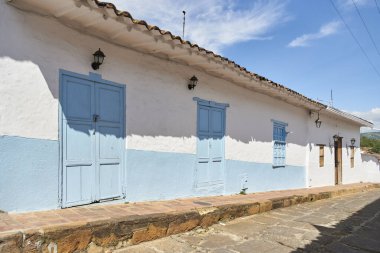 Barichara, Santander, Kolombiya; 25 Kasım 2022: Beyaz ve açık mavi ev, Kolombiya 'nın en güzel köyü olarak bilinen bu turistik kasabanın sömürge kaldırımlı caddesi..