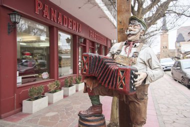 Villa General Belgrano, Cordoba, Argentina; Aug 21, 2024: Figure of a joyful man in traditional Central European clothes laughing playing accordion in a downtown street. clipart