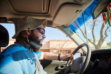 Arabayla seyahat eden ve aracını sürmeye odaklanmış genç bir adamın yan portresi. Otomobilin içinden görüntüle.