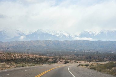Bir yol gezisi sahnesi: Arjantin 'in Mendoza kentindeki karlı And Dağları' nda, ufukta boş bir yolda araba sürmek.