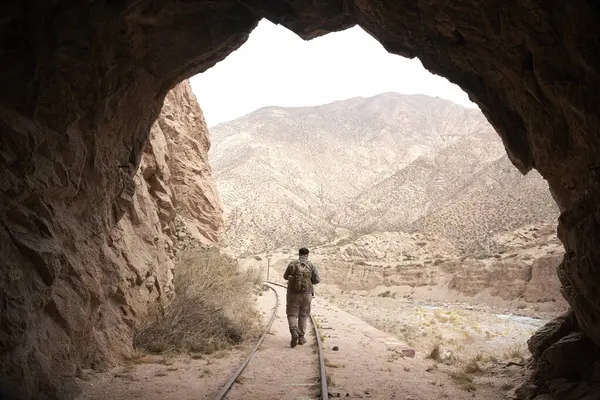 Tren tünelinin çıkışında, dışarıda raylar boyunca yürüyen biri var. Arka planda, bir dağ manzarası. Kavramları: tünelin sonunda ışığı bulmak, gelecek için umut etmek.