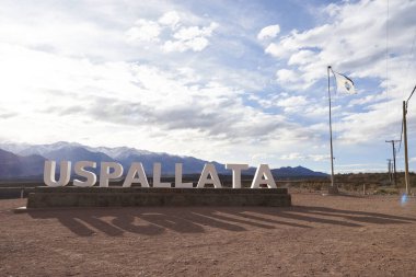 Uspallata, Mendoza, Arjantin; 17 Ağustos 2023: Andean şehrinin adıyla yol kenarı tabelası. Sağ tarafta bir Arjantin bayrağı dalgalanır ve arka planda dağlar belirir..