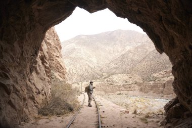 Bir tren tünelinin çıkışında, Arjantin, Mendoza 'daki Andean Dağı manzarasına bakan bir adam var.. 