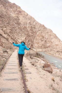 Arjantin 'in Potrerillos kentindeki dağlık bir arazide dengede yürüyen bir kadın görülüyor. Sağda Mendoza Nehri var..