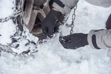 Kış zamanı seyahat et, bir dağ yolunda kar üzerinde ilerleyebilmek için, tanınmayan bir adamın ellerini yakından izle, bir SUV aracının tekerleklerine zincir tak..