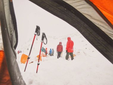 Kış boyunca dağcılık: turuncu bir çadırın içinden dışarıya bakmak: soğuk, kışlık bir dağ manzarası, karla kaplı bir kamp alanındaki insanlar. Mendoza, Arjantin 'deki And sahnesi.