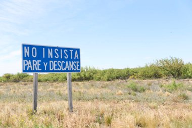 La Pampa, Arjantin; 20 Kasım 2023: Yüksek uykuya dalma riski olan monoton düz yolda sürücüler için uyarı işareti. Metin: Israr etmeyin, durun ve dinlenin.