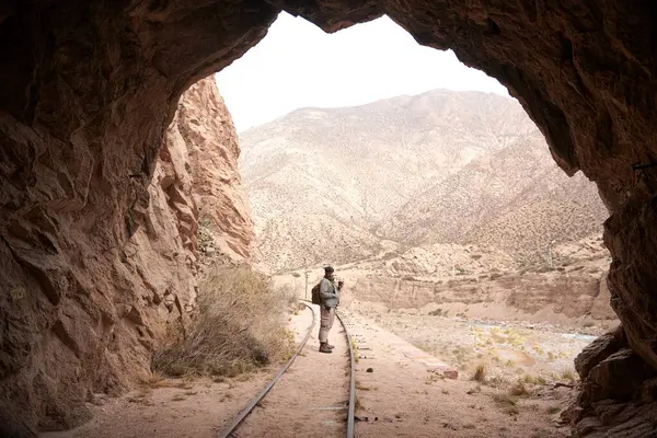Tren tünelinden çıkarken, dışarıda kameraya gülümseyen bir adam var. Arka planda, bir Andean dağı manzarası.