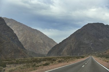 Bir araba gezisi sahnesi: Arjantin, Mendoza 'daki And Dağları' nın kayalık bir manzarasının ortasında boş bir yol..