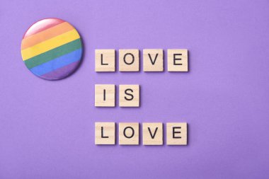 Üzerinde harfler olan tahta parçalar LGBT topluluğunun sembolü olan gökkuşağı bayrağının yanında aşk aşktır yazısını oluşturur. Mor arkaplan, romantik açıdan özgürlüğü ve eşitliği teşvik eden tasarım.