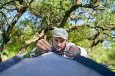 İnsan çadırının kutuplarını bağlamaya odaklanır, doğal, sessiz, yeşil ve güneşli bir ortama kurma sürecinde..
