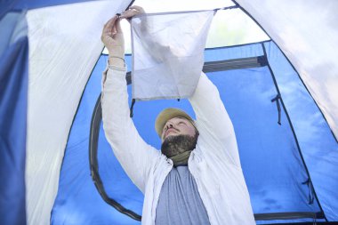 Genç bir erkek gezgin, seyahati sırasında doğal bir bölgede kamp yapmak için mavi bir çadır kuruyor..