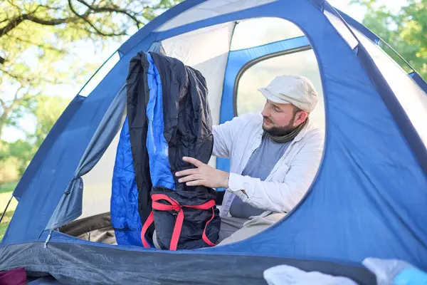 Genç İspanyol gezgin, mavi çadırının içinde kamp yaparken uyku tulumunu çıkartıyor..