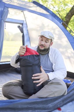 Genç İspanyol gezgin, mavi çadırının içinde kamp yaparken uyku tulumunu çıkartıyor. Onun ifadesi sakin ve sağlıklı..