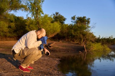 İspanyol gezgin, güneşin ilk ışıklarıyla aydınlanan sakin doğal bir manzarada, gün doğumunda ellerini ve yüzünü bir derenin kıyısında yıkıyor. El Palmar Ulusal Parkı, Entre Rios, Arjantin.