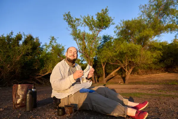 Şafak vakti bir derenin kıyısında oturan gezgin, tipik bir Arjantin içkisi olan eş içmeye hazırlanırken olumlu bir ifadeyle ilk güneş ışınlarını alıyor. El Palmar Ulusal Parkı.