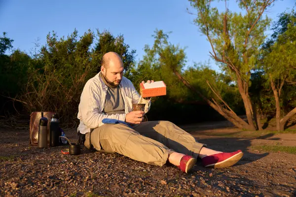 Şafak vakti bir derenin kıyısında oturan gezgin, tipik bir Arjantin içkisi olan eşi içmeye hazırlanırken ilk güneş ışınlarını alıyor. El Palmar Ulusal Parkı, Entre Rios, Arjantin.