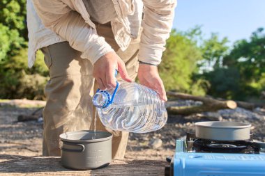 Kamp yaparken yemek pişirme sürecinin bir parçası olarak, tanınmayan kişi bir tencereye içme suyu döküyor..