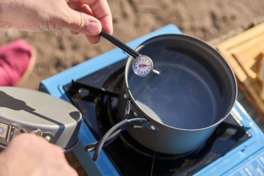 Tanınmayan bir adam, portatif kamp sobası kullanarak tencerede ısıttığı suyun sıcaklığını ölçüyor..