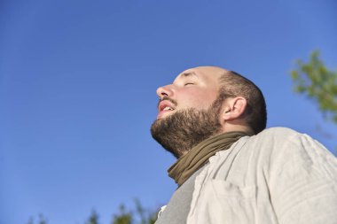 Sakin ve barışçıl bir ifadeyle gülümseyen genç bir adamın samimi portresi. Sabah güneşiyle aydınlanıyor. Sahne, refahı, sükuneti ve olumlu duyguları yansıtıyor. Düşük açı görünümü.