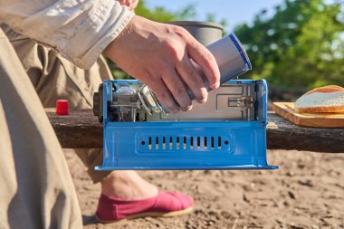 Gezisi sırasında yemek pişirmek için mavi portatif bir kamp sobasının üzerine gaz kutusu koyan tanınmamış biri..