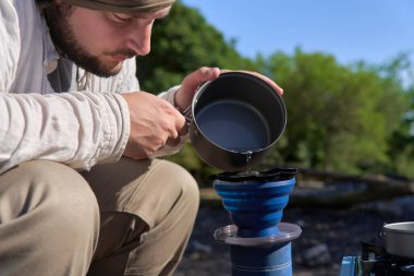 Açık hava kahve yapma süreci: İspanyol bir gezgin kahvaltısını hazırlamak için taze öğütülmüş kahve içeren katlanmış seyahat filtresine sıcak su döker.
