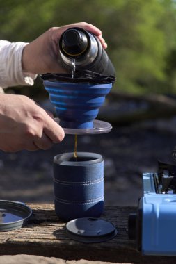 Açık hava kahve yapma süreci: tanınmayan bir gezgin kahvaltısını hazırlamak için içinde taze öğütülmüş kahve bulunan katlanmış seyahat filtresine sıcak su döker.